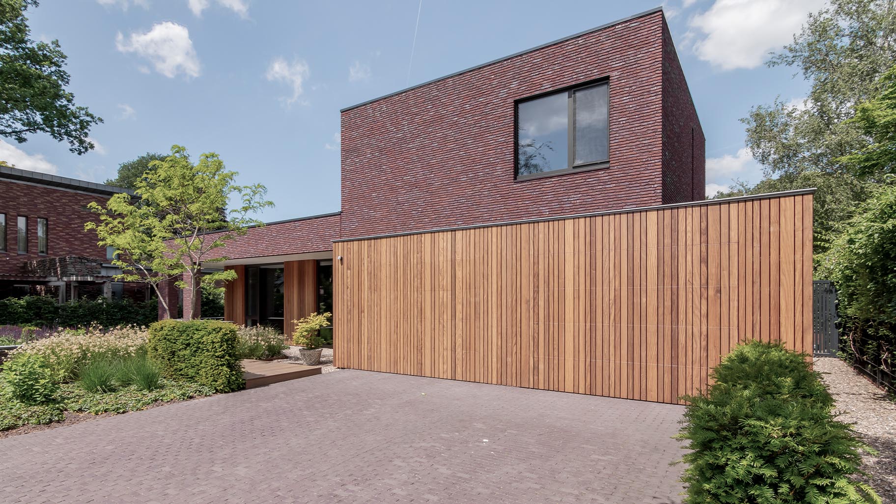 De houten garagedeuren zijn onopvallend ingebouwd in het ontwerp van de gevelbekleding