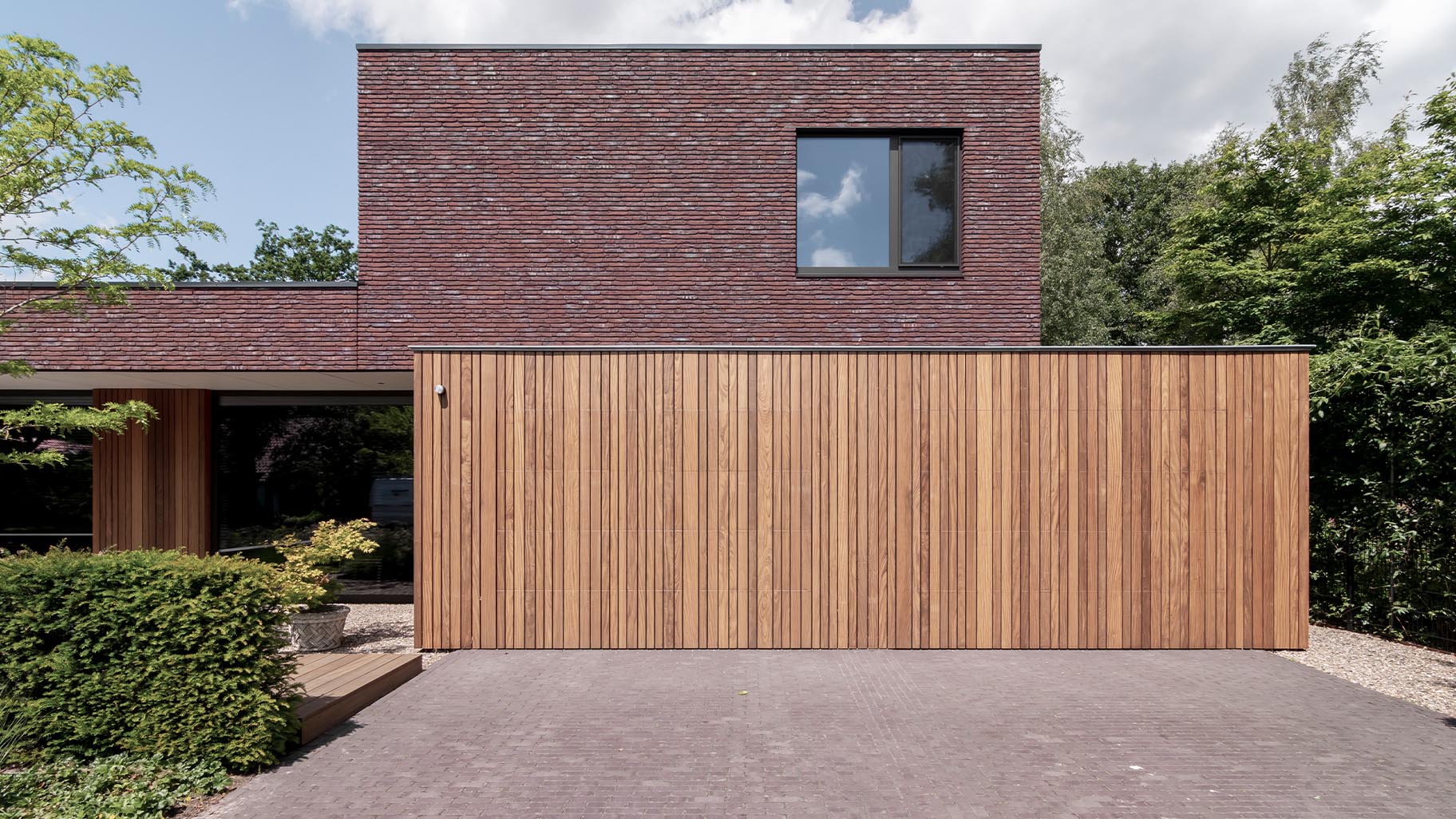 De houten garagedeuren zijn onopvallend ingebouwd in het ontwerp van de gevelbekleding
