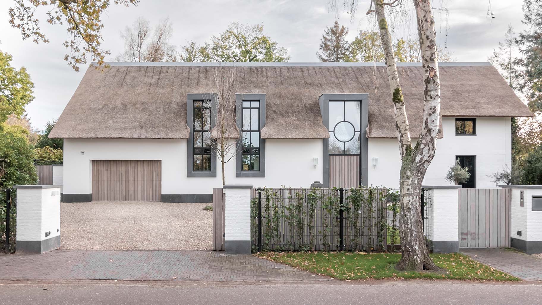 Houten garagedeur achter de dag geïntegreerd in de gevel van een landelijke woning met rieten dak
