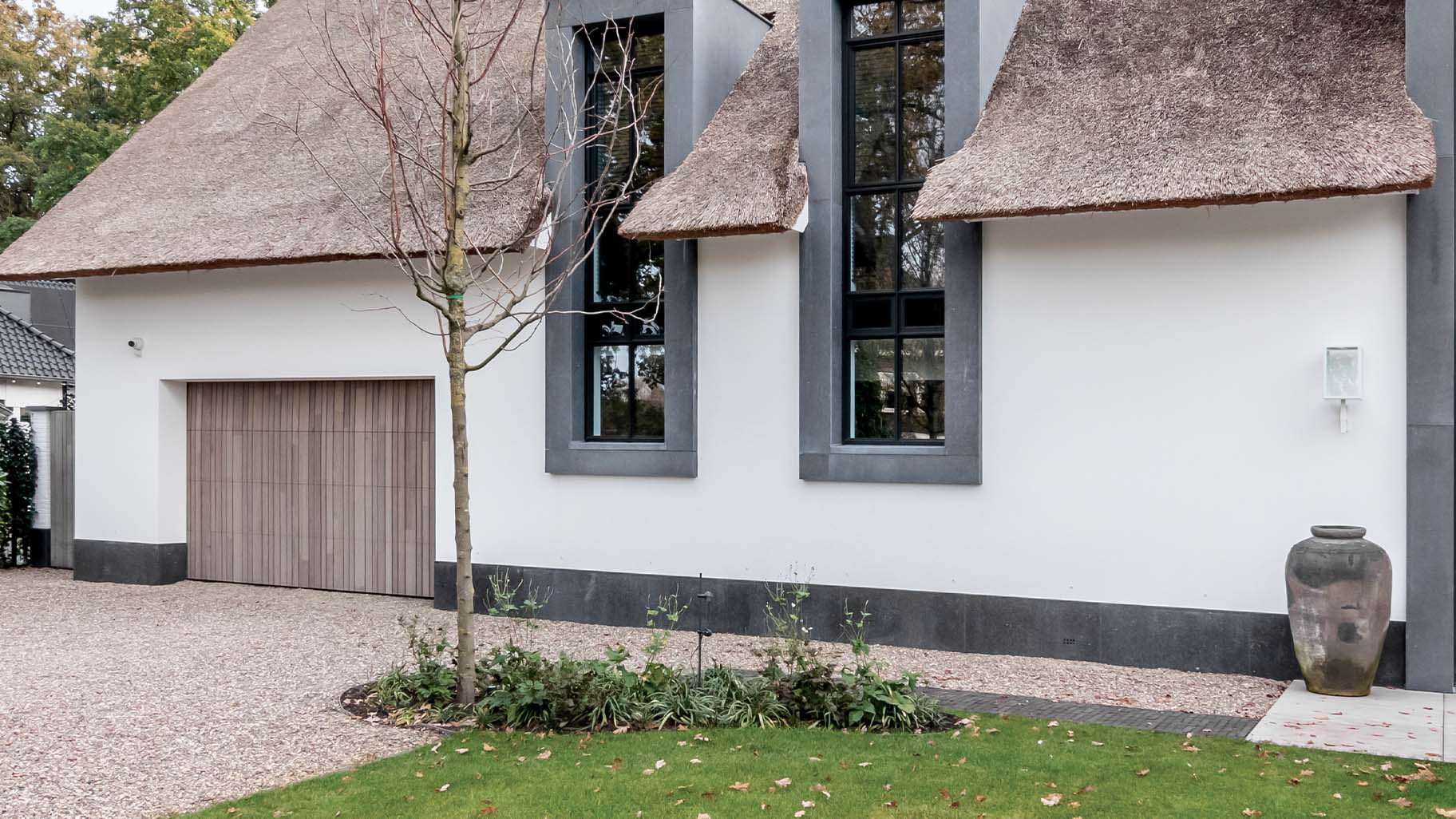 Houten garagedeur achter de dag geïntegreerd in de gevel van een landelijke woning met rieten dak