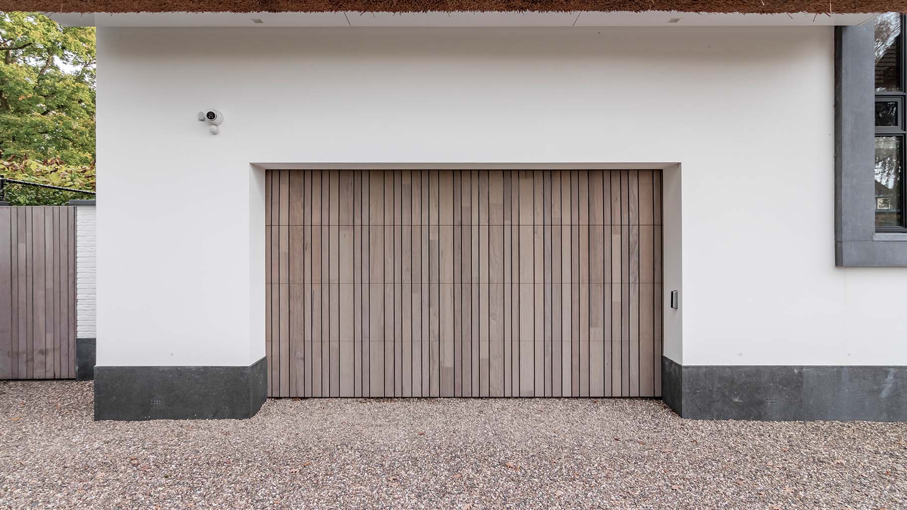 Different Doors houten garagedeur achter de dag, passend bij landelijke woning met rieten dak