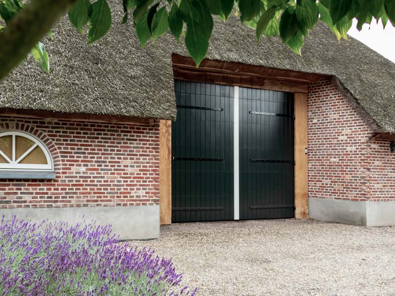 Boerderij met rieten dak en openslaande houten garagedeur, passend bij landelijke uitstraling