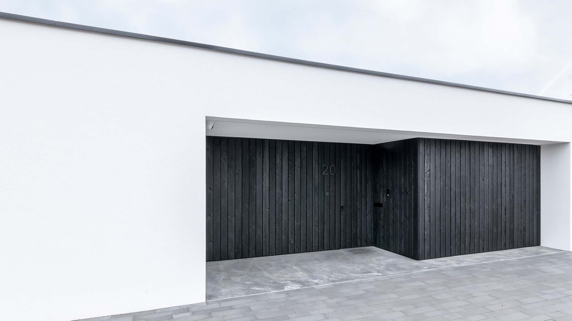 Moderne woning met Shou Sugi Ban houten garagedeur en voordeur, gelijk met de zwarte gevel