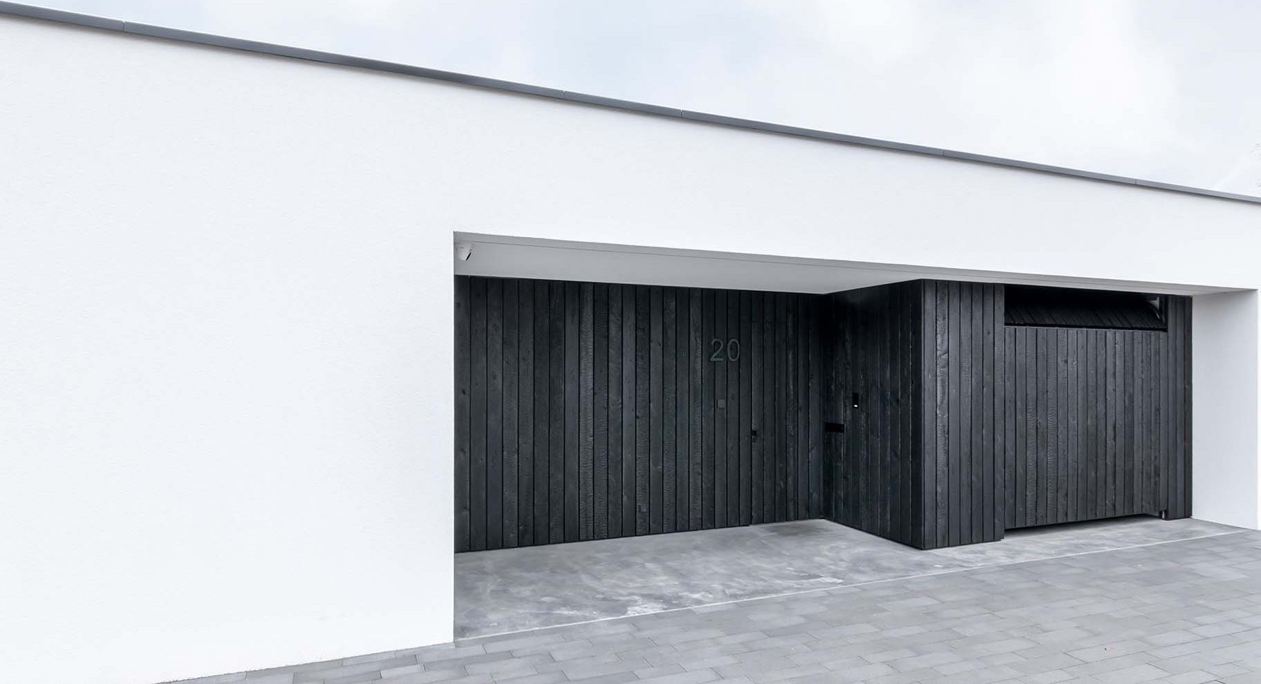 Moderne woning met Shou Sugi Ban houten garagedeur en voordeur, gelijk met de zwarte gevel