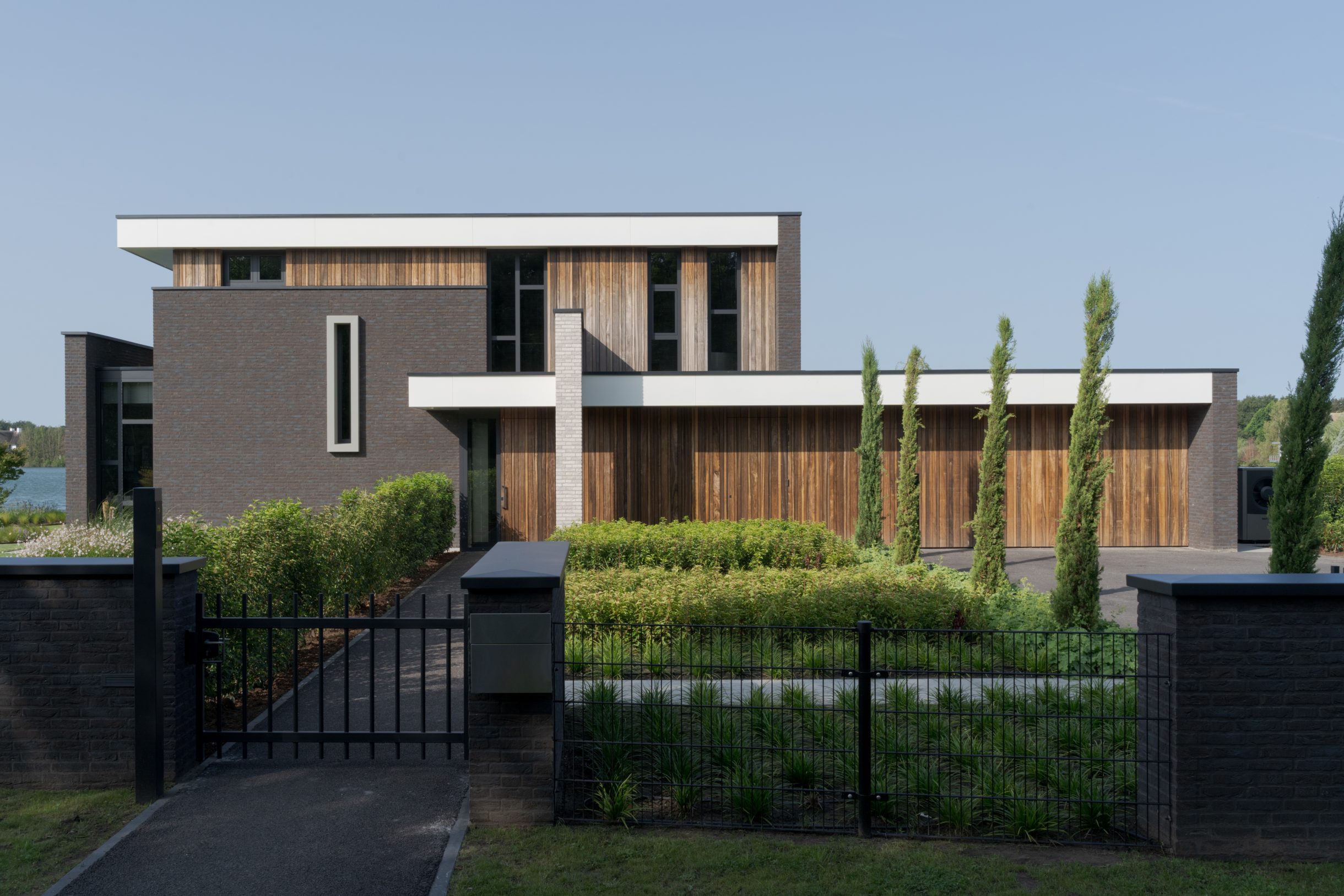 Twee houten garagedeuren uitgevoerd in padoek en perfect geïntegreerd in de verticale houten latten bij deze prachtige nieuwbouwwoning aan het water