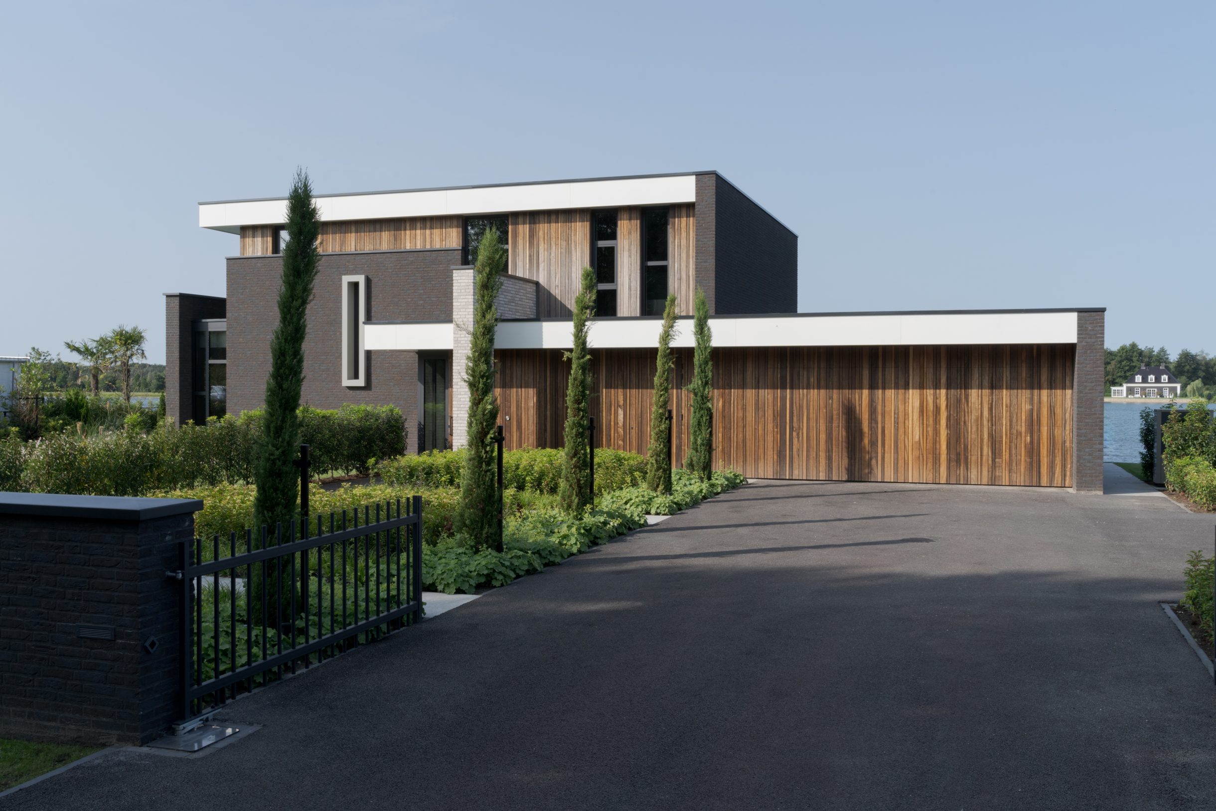 Twee houten garagedeuren uitgevoerd in padoek en perfect geïntegreerd in de verticale houten latten bij deze prachtige nieuwbouwwoning aan het water