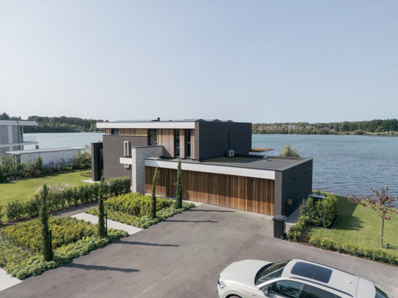 Twee houten garagedeuren uitgevoerd in padoek en perfect geïntegreerd in de verticale houten latten bij deze prachtige nieuwbouwwoning aan het water