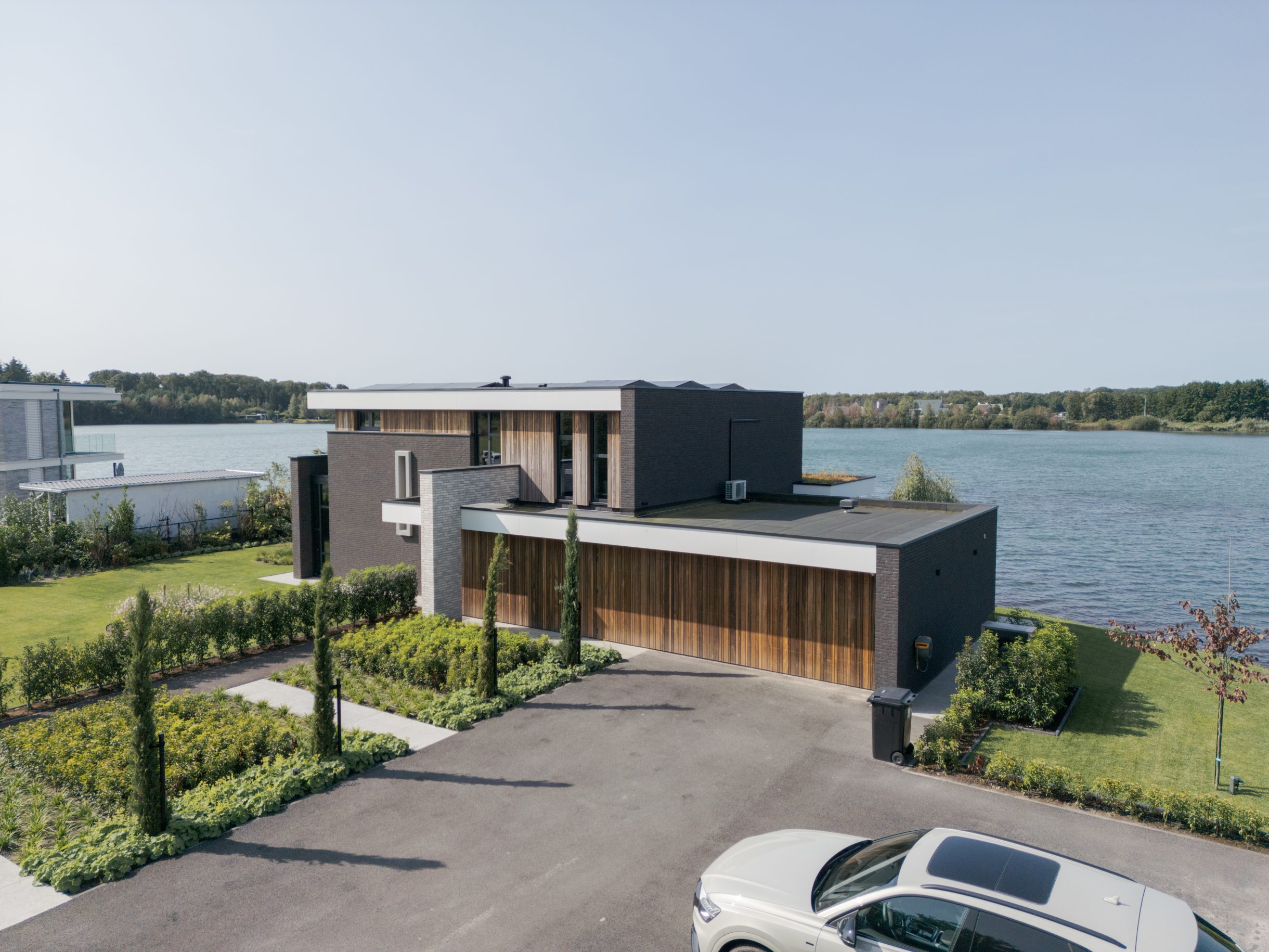 Twee houten garagedeuren uitgevoerd in padoek en perfect geïntegreerd in de verticale houten latten bij deze prachtige nieuwbouwwoning aan het water