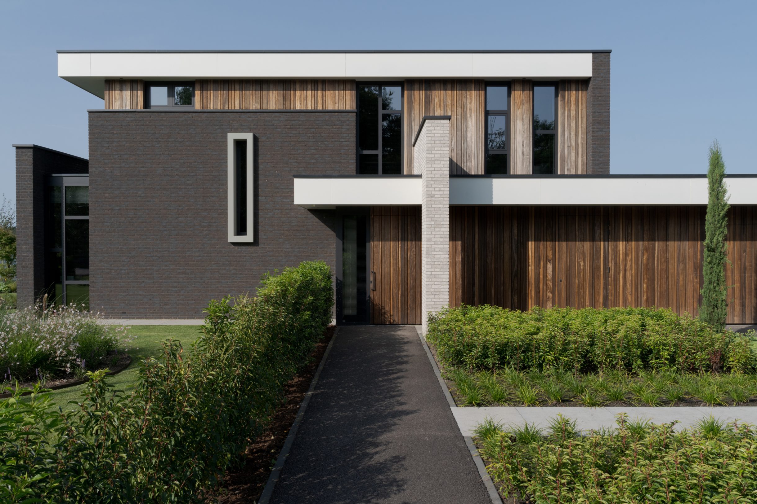 Twee houten garagedeuren uitgevoerd in padoek en perfect geïntegreerd in de verticale houten latten bij deze prachtige nieuwbouwwoning aan het water