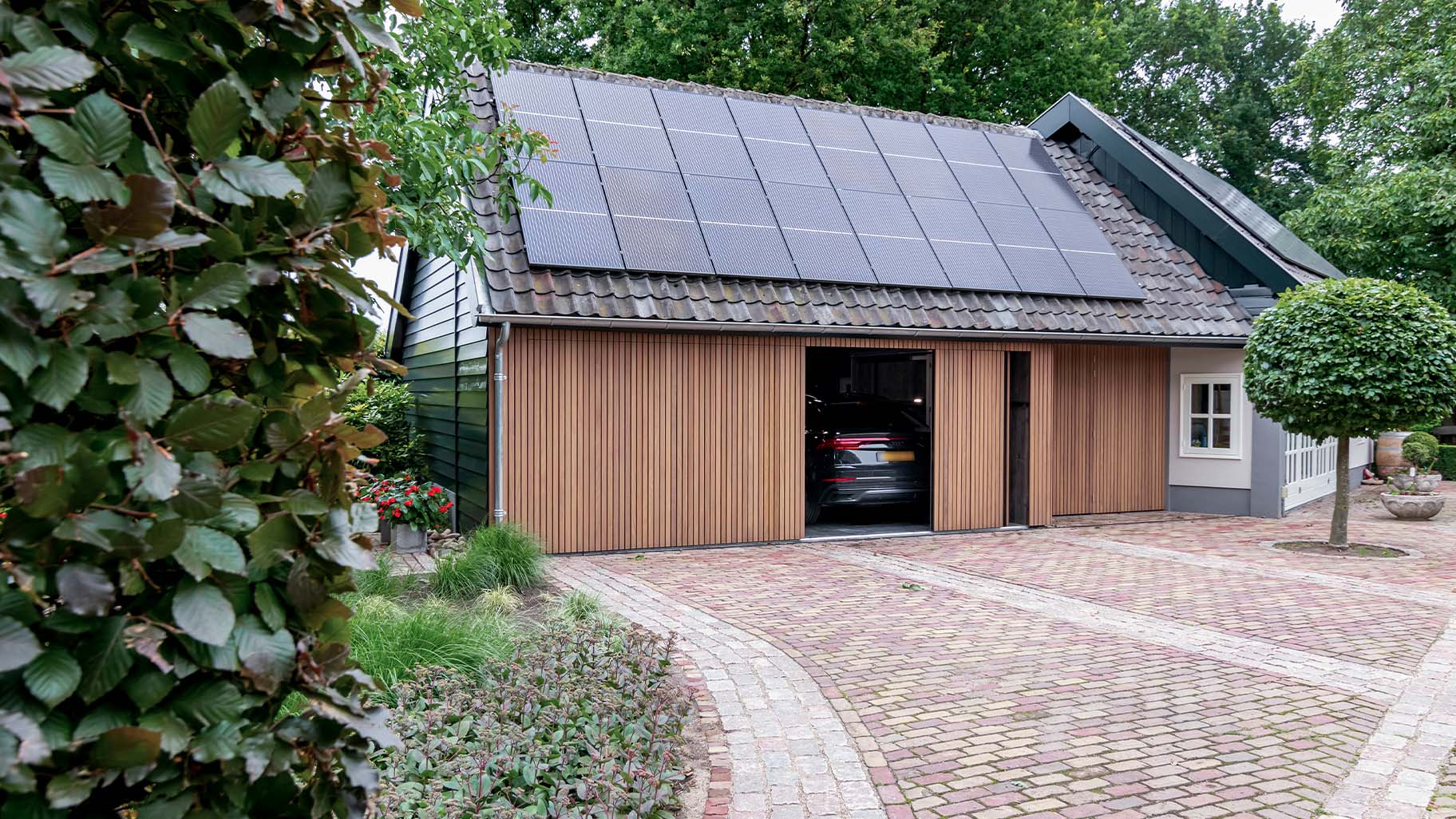 Gevelrenovatie van boerderij met een nieuwe zijwaartse houten garagedeur met dunne latjes
