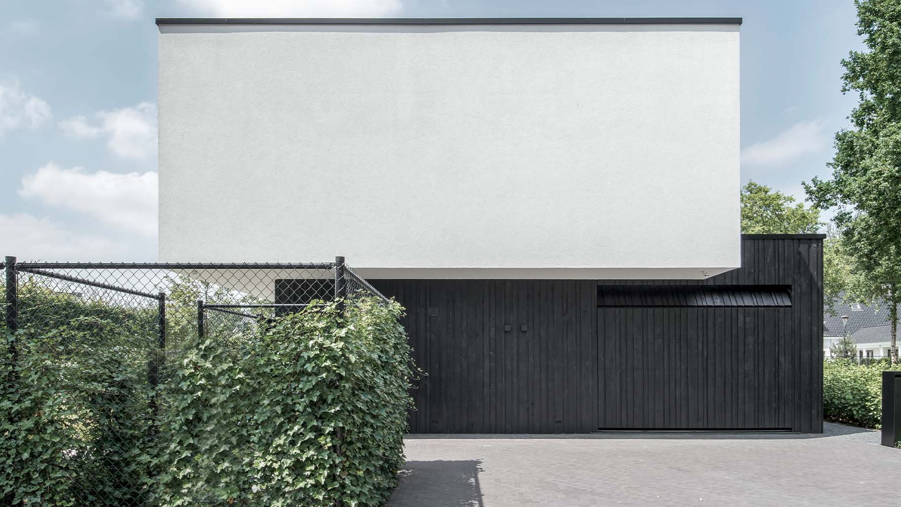 Moderne zwarte garagedeur met verticale houten latten in diverse breedtes, contrasterend met witte gevel