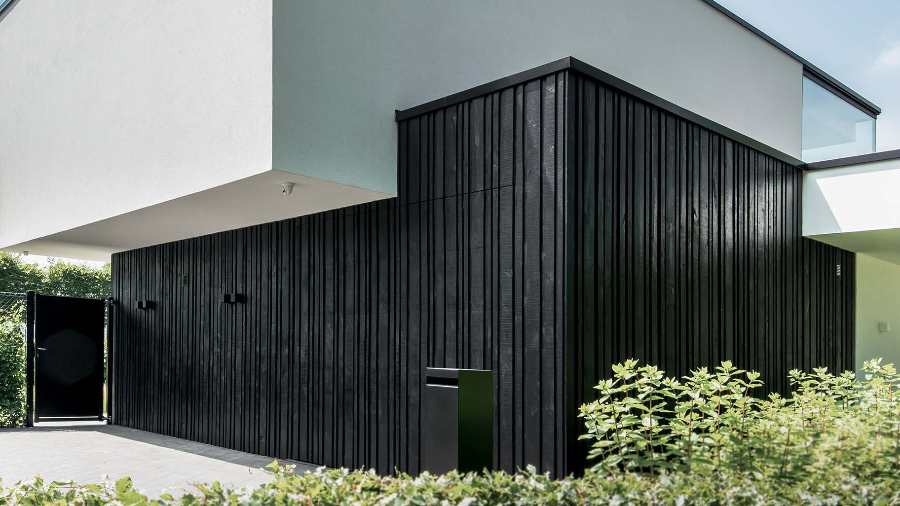 Moderne zwarte garagedeur met verticale houten latten in diverse breedtes, contrasterend met witte gevel