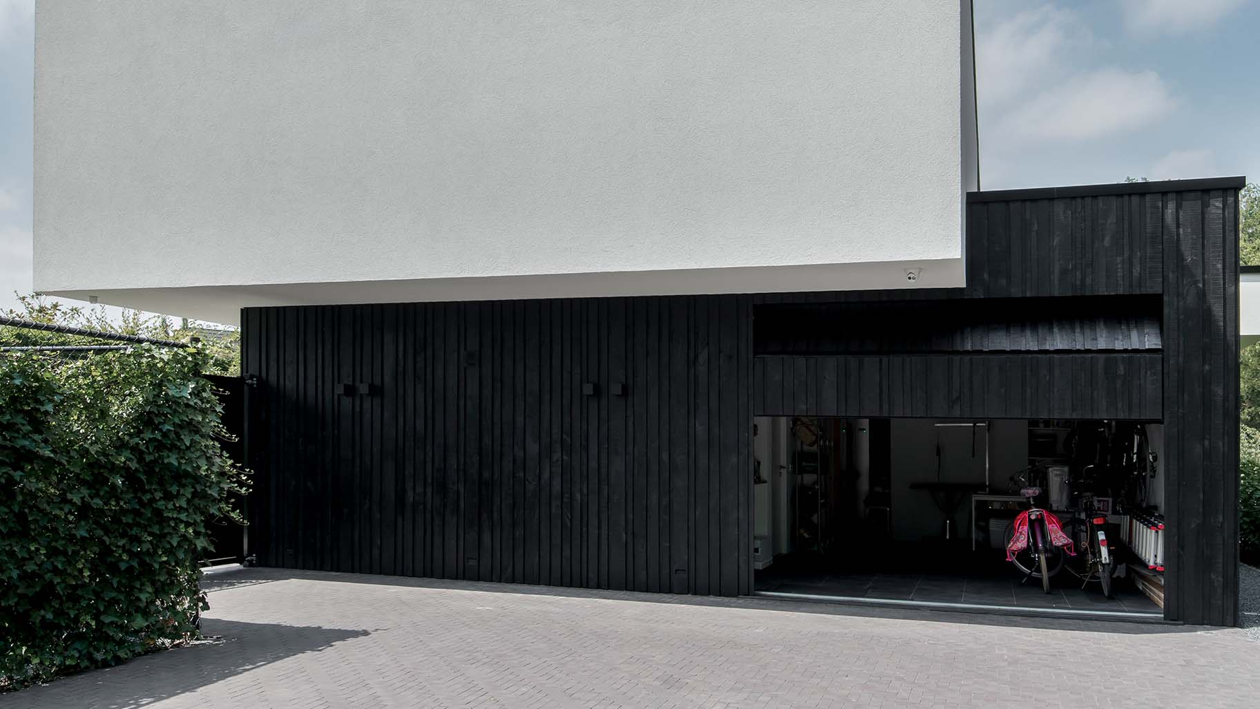 Moderne zwarte garagedeur met verticale houten latten in diverse breedtes, contrasterend met witte gevel