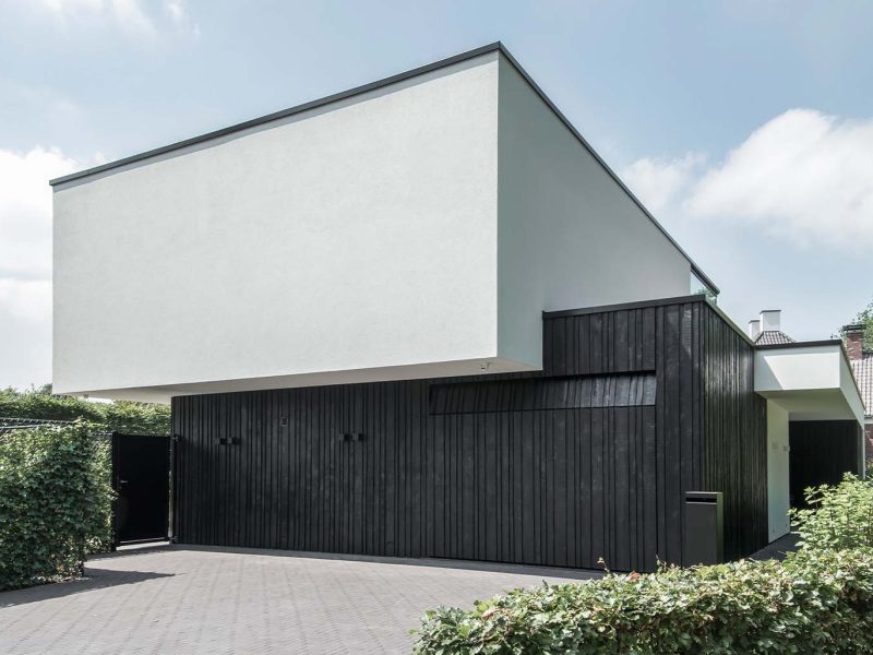 Moderne zwarte garagedeur met verticale houten latten in diverse breedtes, contrasterend met witte gevel