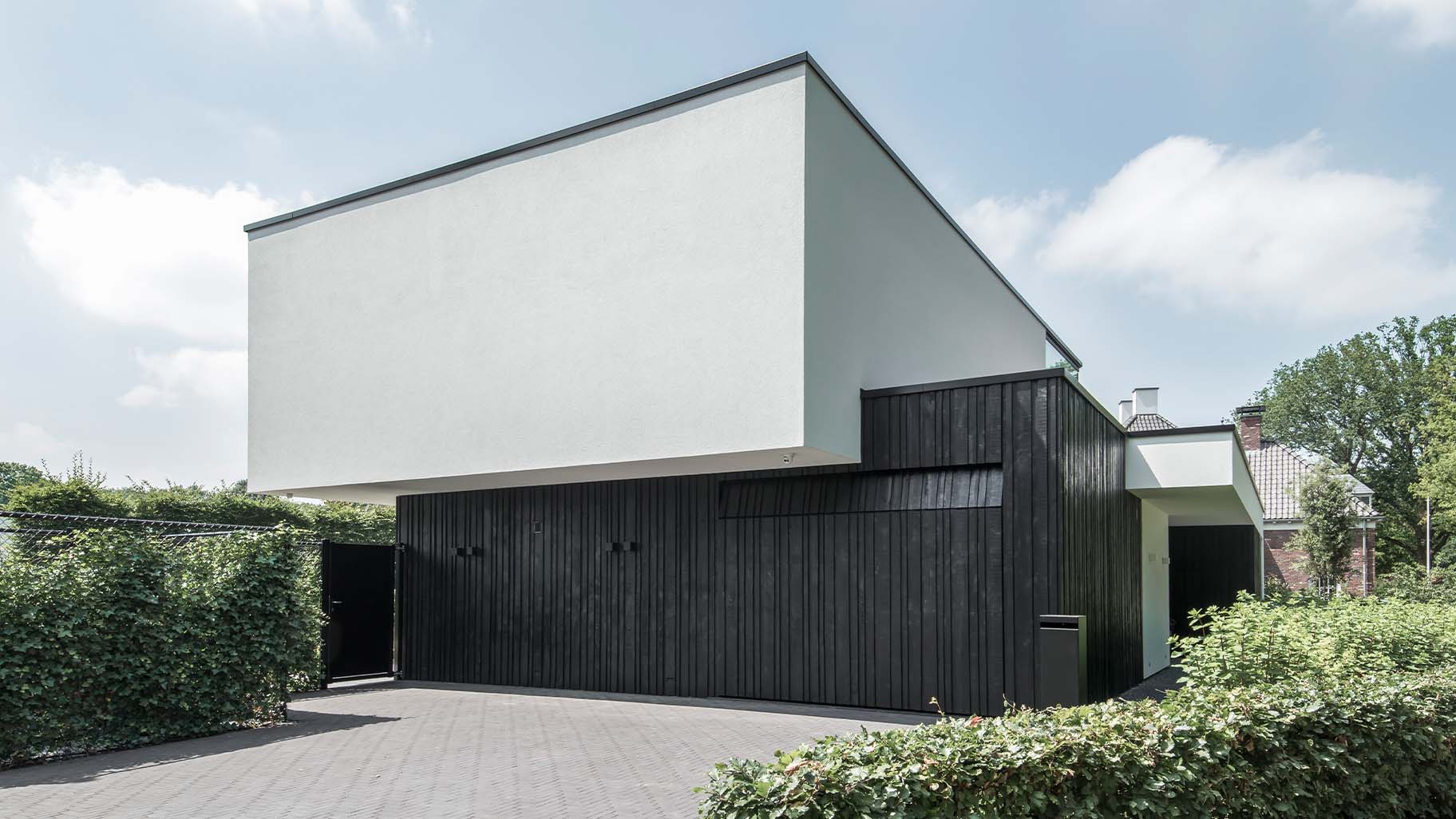 Moderne zwarte garagedeur met verticale houten latten in diverse breedtes, contrasterend met witte gevel