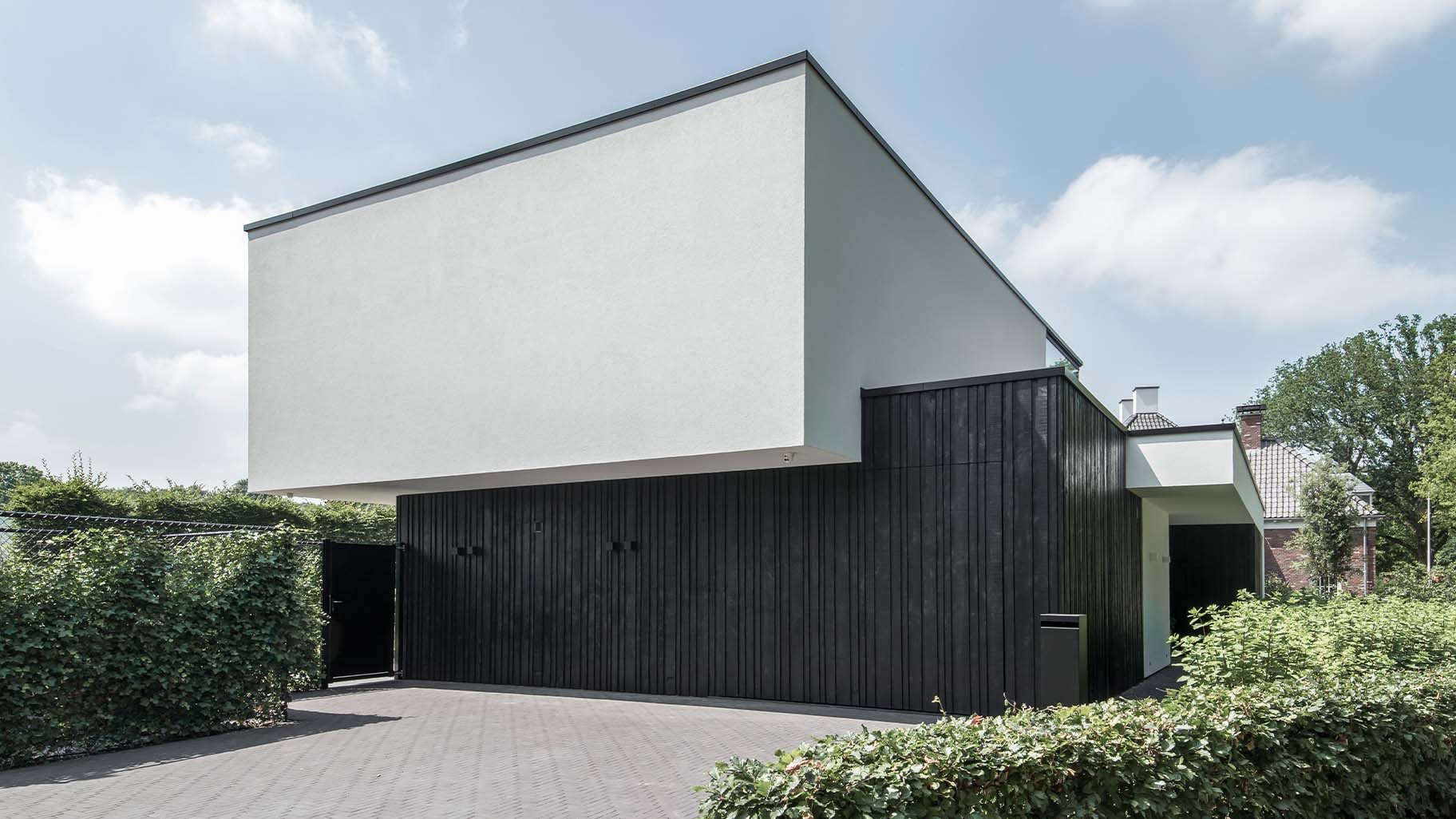 Moderne zwarte garagedeur met verticale houten latten in diverse breedtes, contrasterend met witte gevel