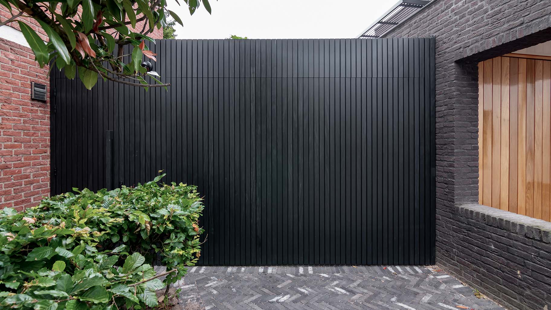 Op maat gemaakte zwarte houten zijwaartse garagedeur, gerealiseerd door Different Doors